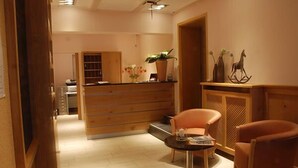 Un espace d’accueil comprenant un bureau en bois, deux chaises, une petite table avec un magazine et une plante.