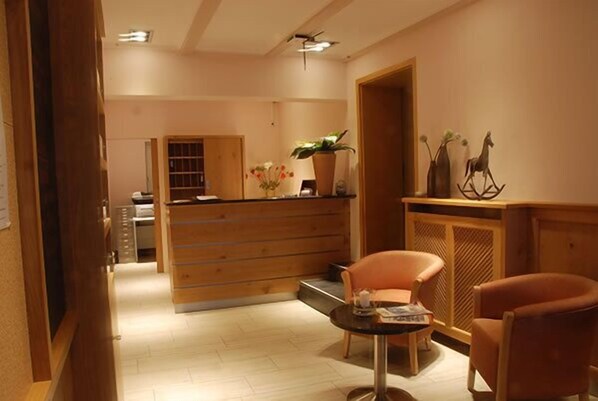 A reception area with a wooden desk, two chairs, a small table with a magazine, and a plant.
