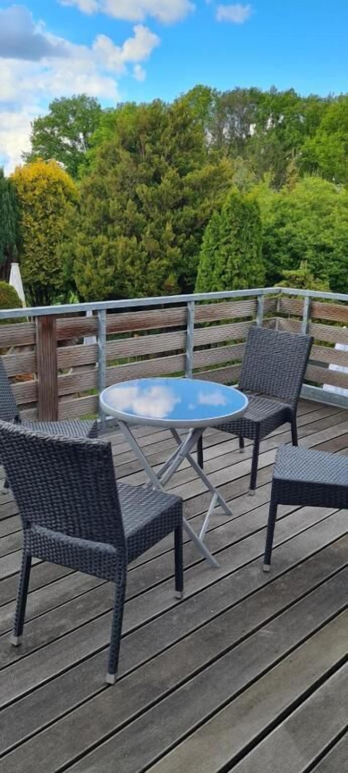A wooden deck with a round table and four wicker chairs.