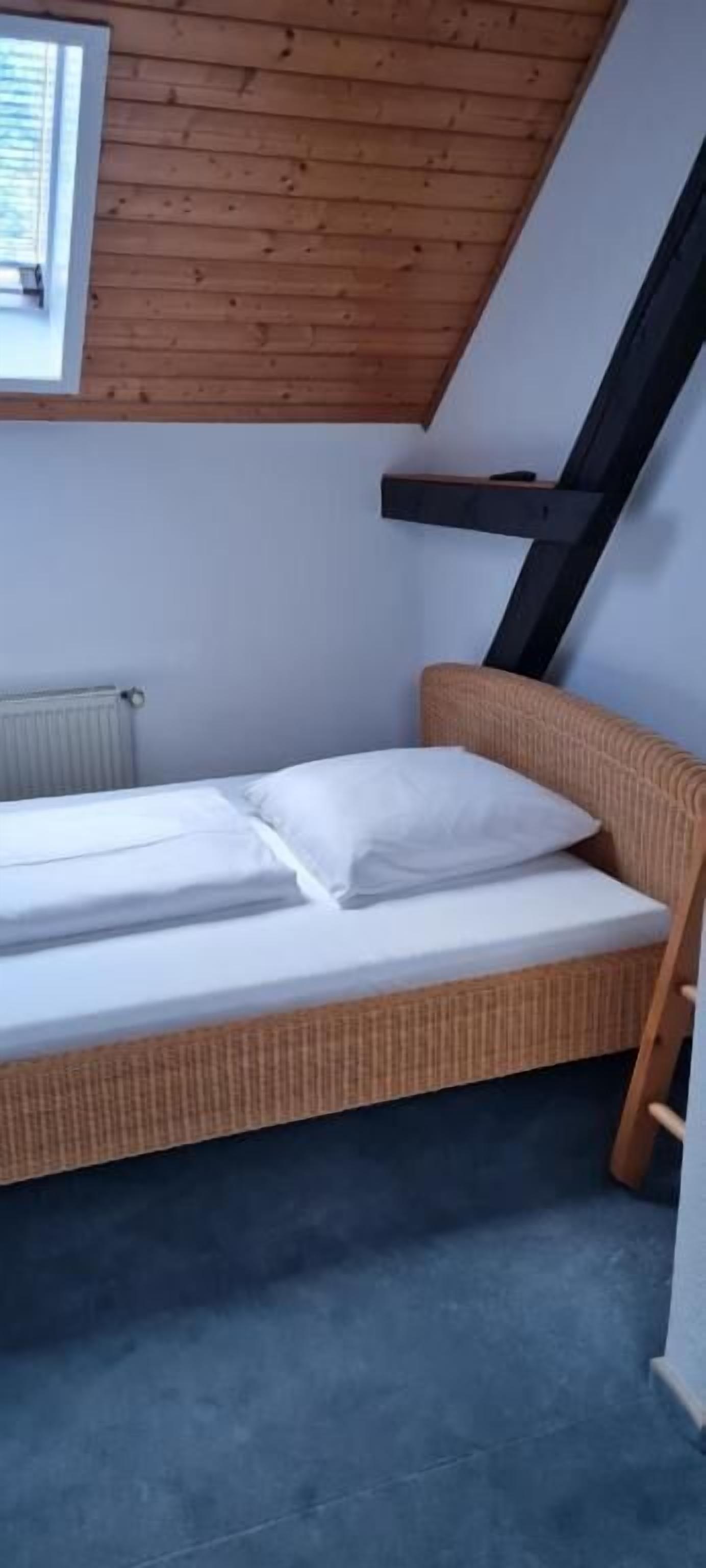 Une petite chambre avec un lit simple, un plafond en pente et une fenêtre.