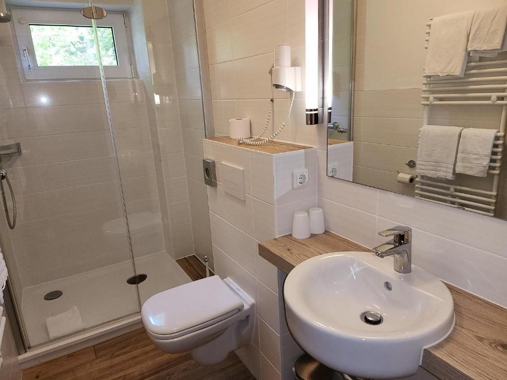 Un baño con ducha envuelta en vidrio, inodoro blanco, lavabo con encimera de madera y espejo con toallero.