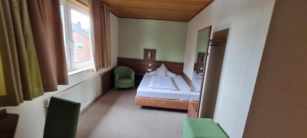 Un dormitorio con una cama individual, una silla, un aparador y una ventana con cortinas.