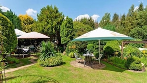 Un jardin bien entretenu, agrémenté d’espaces de détente en plein air abrités par des parasols, et entouré d’une végétation luxuriante et d’arbres.