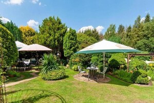 Un jardín bien cuidado con zonas de estar al aire libre bajo sombrillas, rodeado de abundante vegetación y árboles.