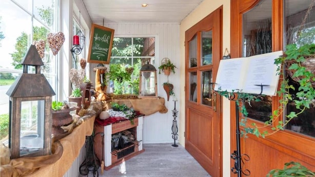 Un couloir chaleureux et bien éclairé, avec des portes en bois, un piano et diverses plantes.