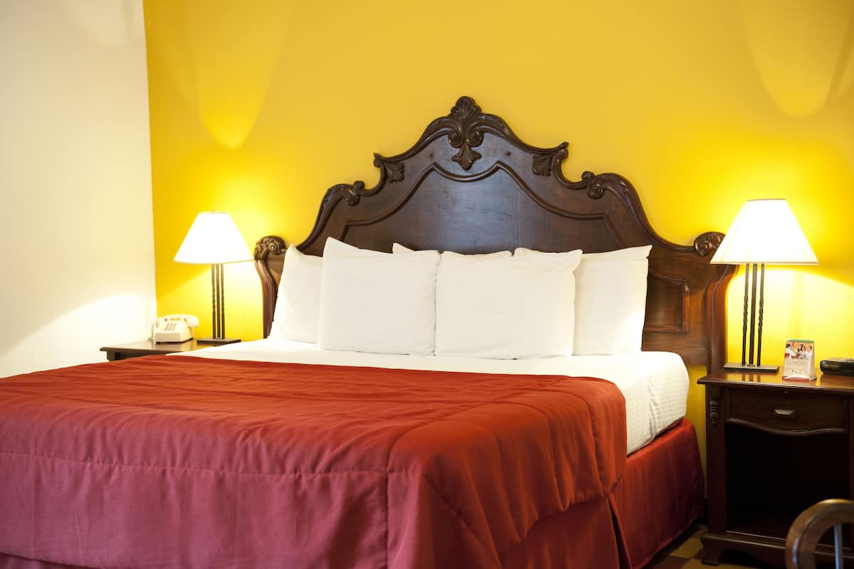 A bed with a wooden headboard, white bedding, and a red bedspread. There are two bedside tables with lamps and a telephone on one.