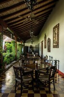 Un comedor con mesas y sillas de madera, piso a cuadros, ventilador de techo y pared decorada con cuadros.