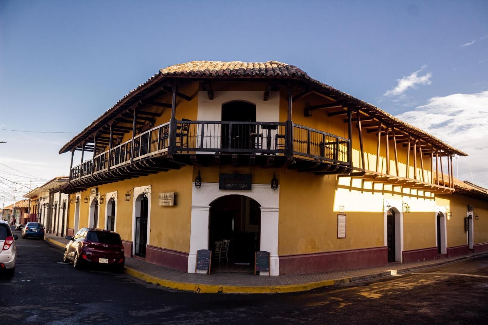 Un edificio de estilo colonial amarillo con balcón, arcos y tejado de tejas.