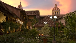 Um pátio com jardim, um edifício com cúpula e um campanário.