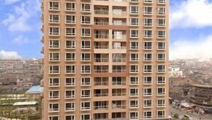 Een hoog woongebouw met meerdere balkons, een centrale ingang en aangelegde tuinen.