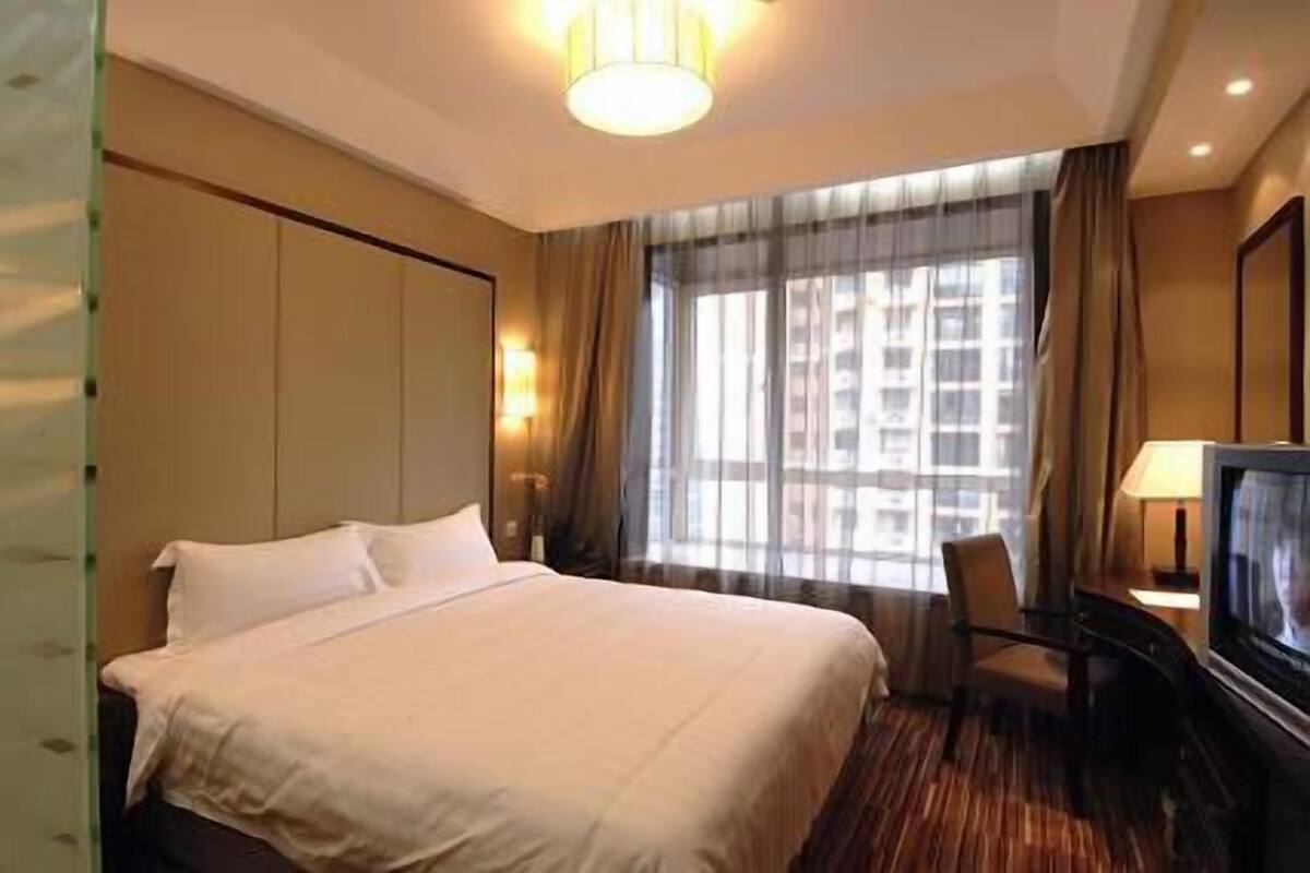 Een hotelkamer met een groot bed, een bureau met een televisie en een raam met gordijnen.