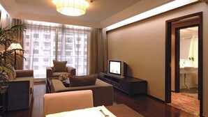Een moderne hotelkamer met een zithoek, een eettafel met bord en bestek, een televisie en een groot raam met gordijnen.