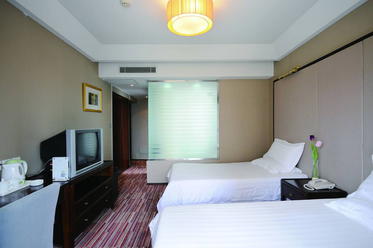 Hotelkamer met twee bedden, een televisie, een bureau met telefoon en een raam met luxaflex.