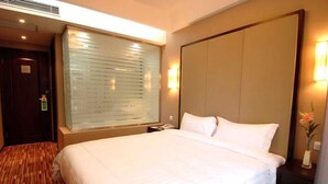 Een hotelkamer met een groot bed, een raam met zonwering, een nachtkastje met een lamp en een deur.
