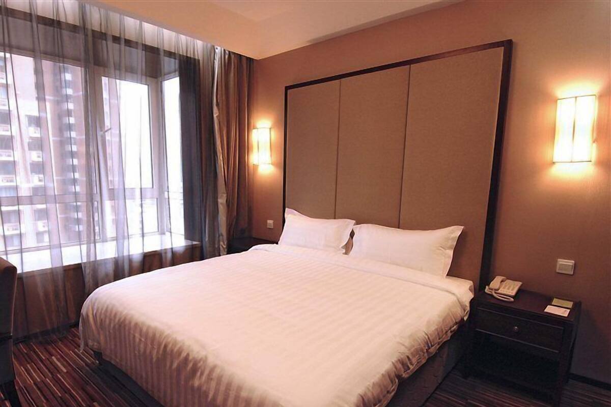 Een hotelkamer met een groot bed, een nachtkastje met telefoon en een raam met gordijnen.