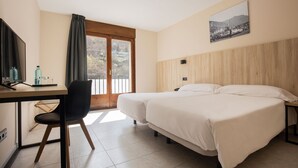 Habitación de hotel con dos camas, un escritorio con silla, televisor y ventana con vista a las montañas.