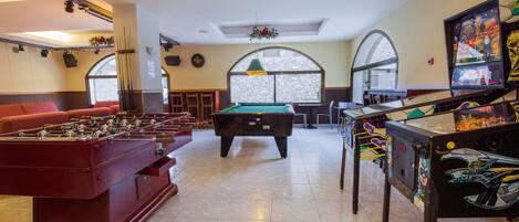 A billiards room with a pool table, foosball table, and pinball machine.