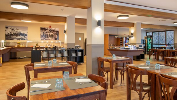 Un restaurante con mesas y sillas de madera, una zona de bufé y una cocina al fondo.