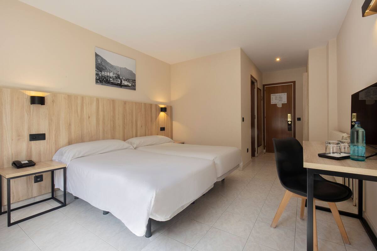A hotel room with a bed, bedside table, desk, chair, and a wall-mounted picture.