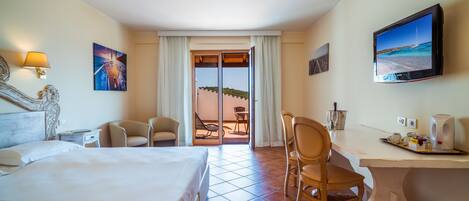 A hotel room with a bed, a desk, a chair, a television, and a view of the beach through the door.