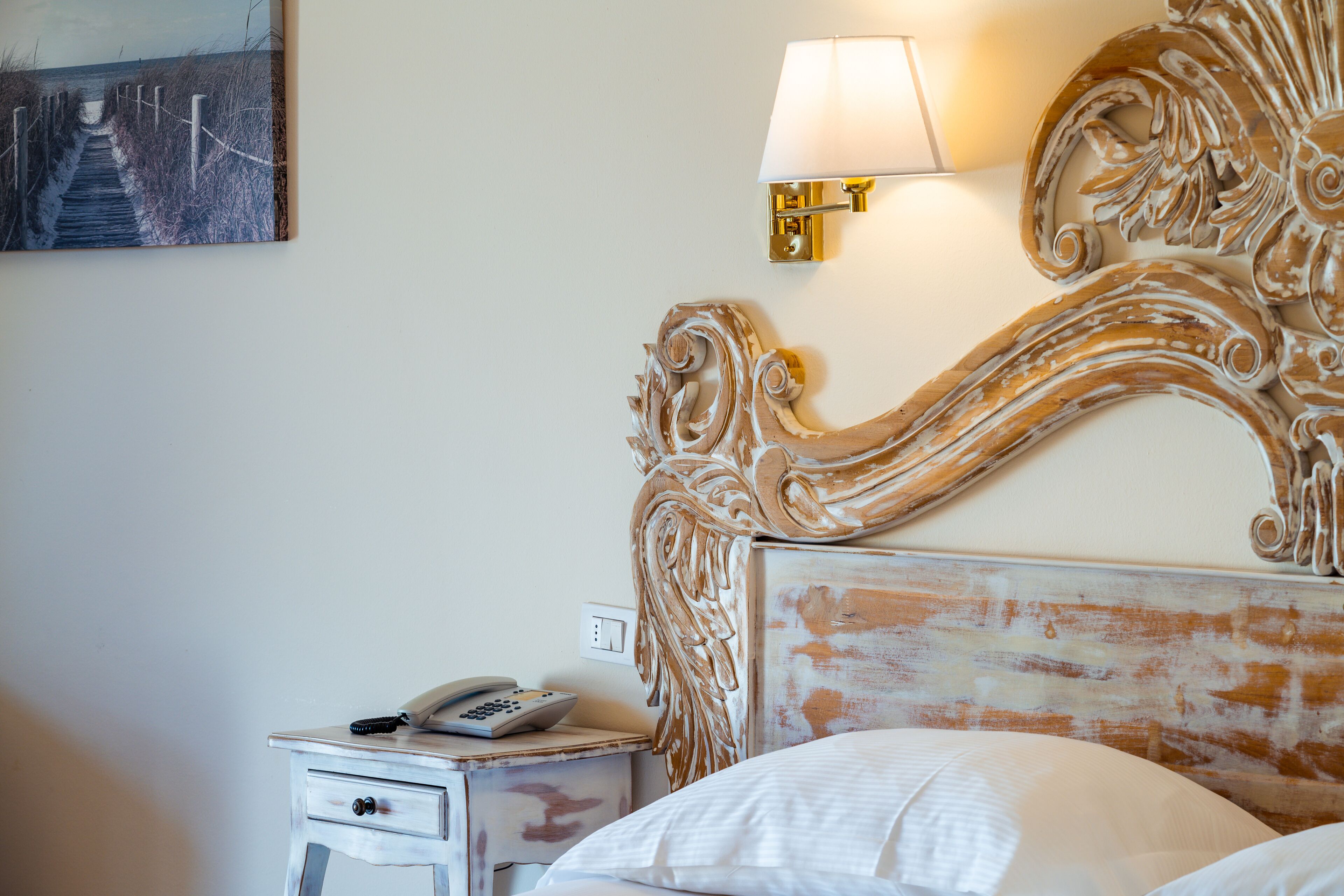 A bedroom with a wooden headboard, a bedside table with a lamp, and a painting on the wall.