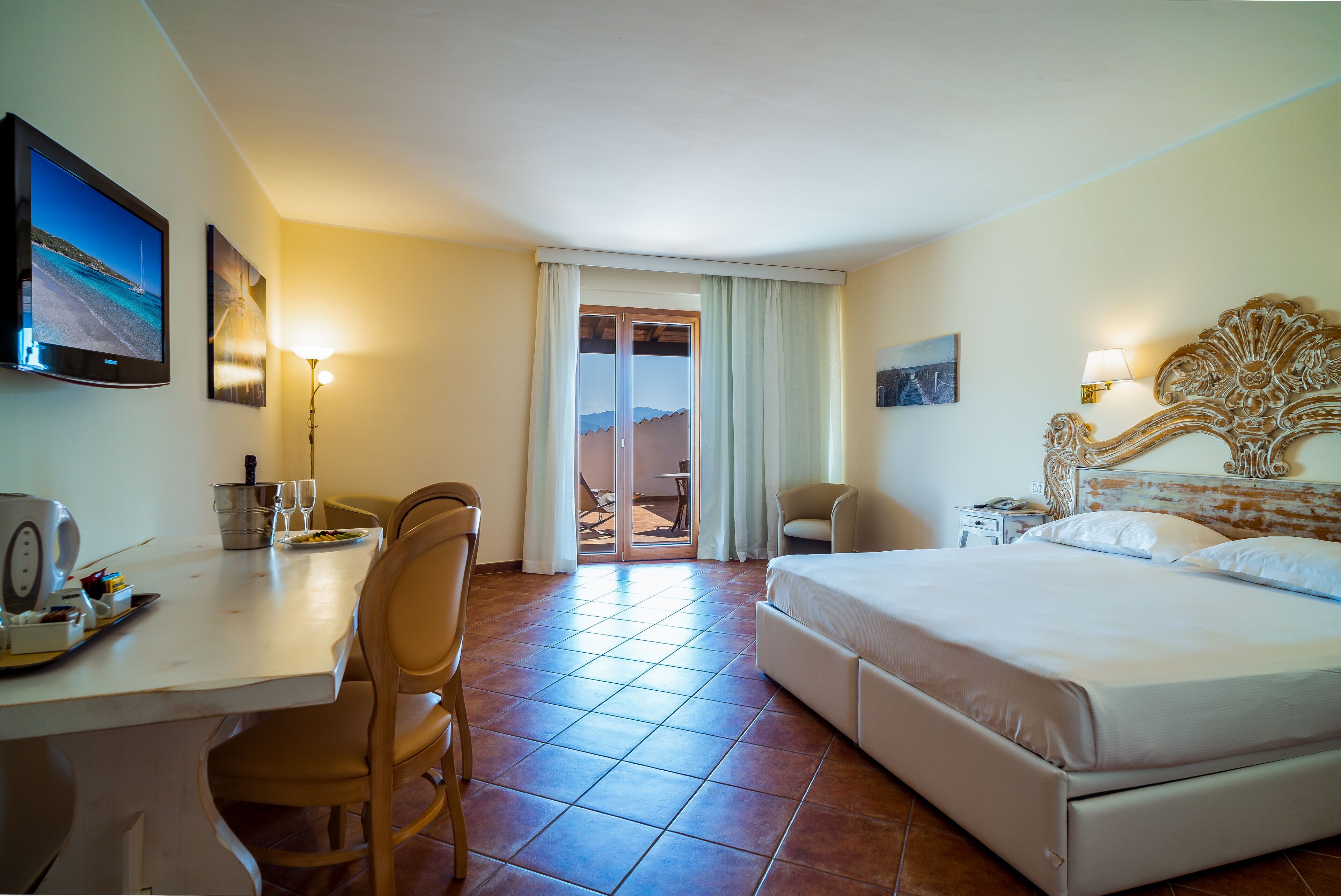 A hotel room with a bed, desk, chairs, and a television.