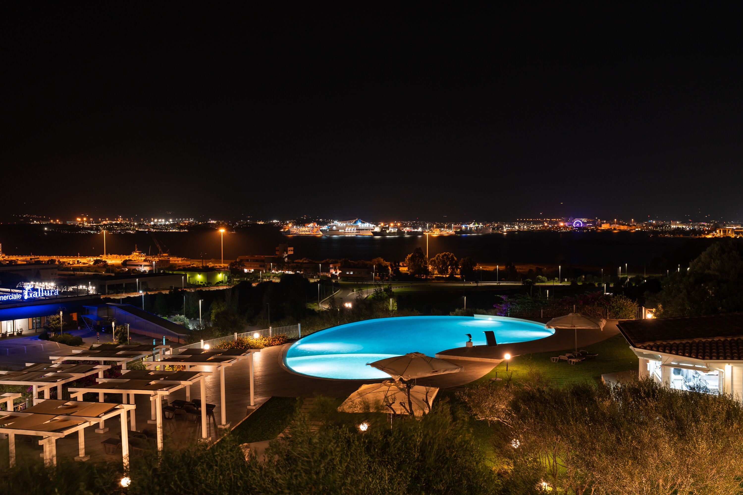 Vista nocturna de un área de piscina con un paisaje urbano de fondo.