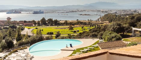 A pool with lounge chairs, a landscaped garden, and a view of a cityscape and mountains in the background.