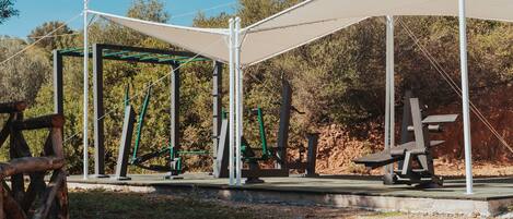 An outdoor gym with exercise equipment and a canopy structure.