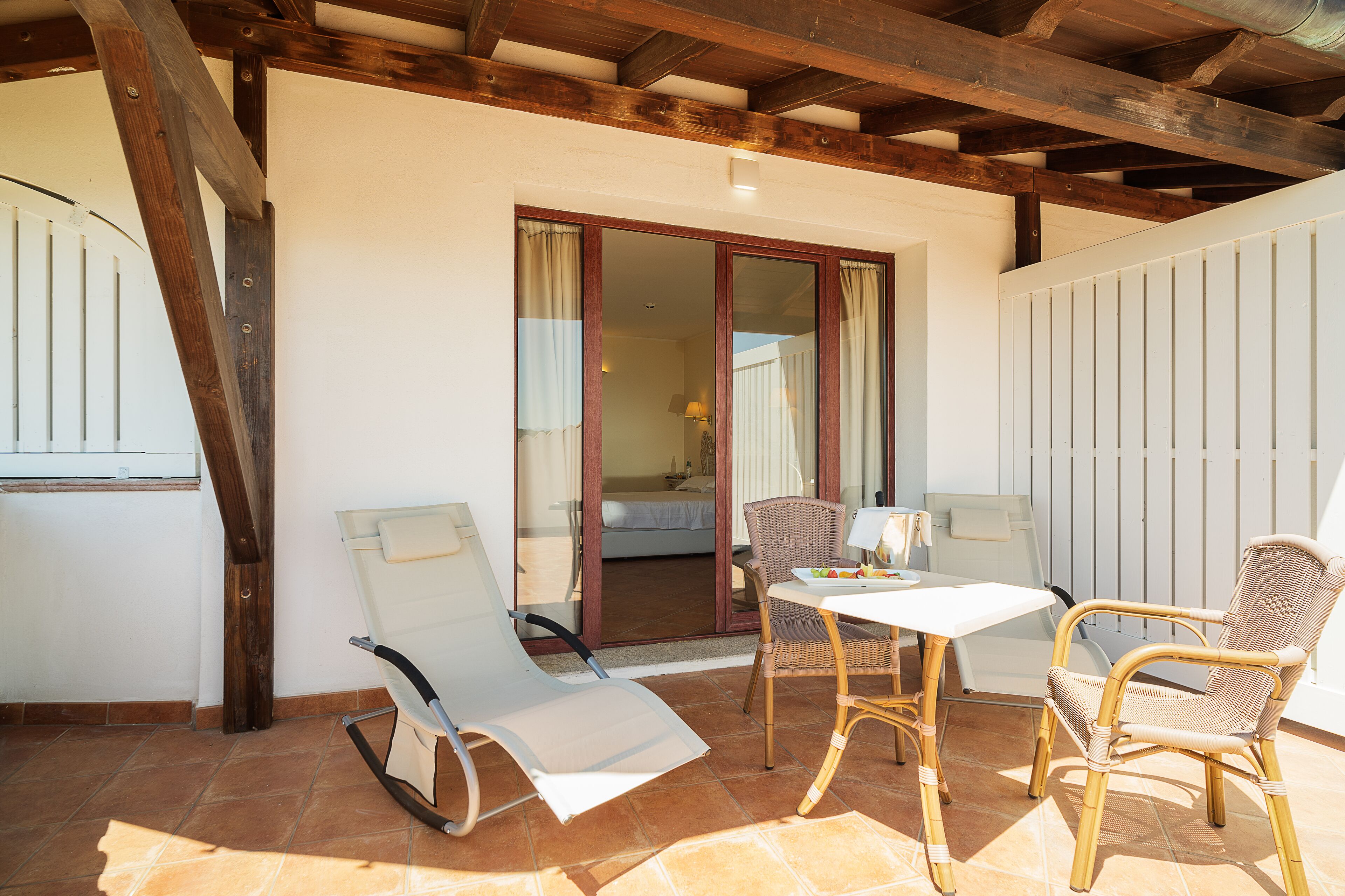 Un patio con mesa y sillas, una puerta corrediza de vidrio que da a un dormitorio y un techo de madera.