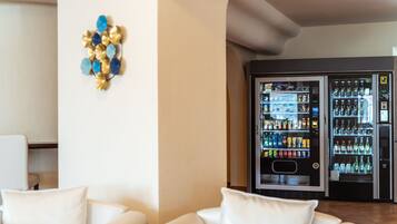 A hotel lobby with a seating area, a decorative wall piece, and a row of beverage vending machines.