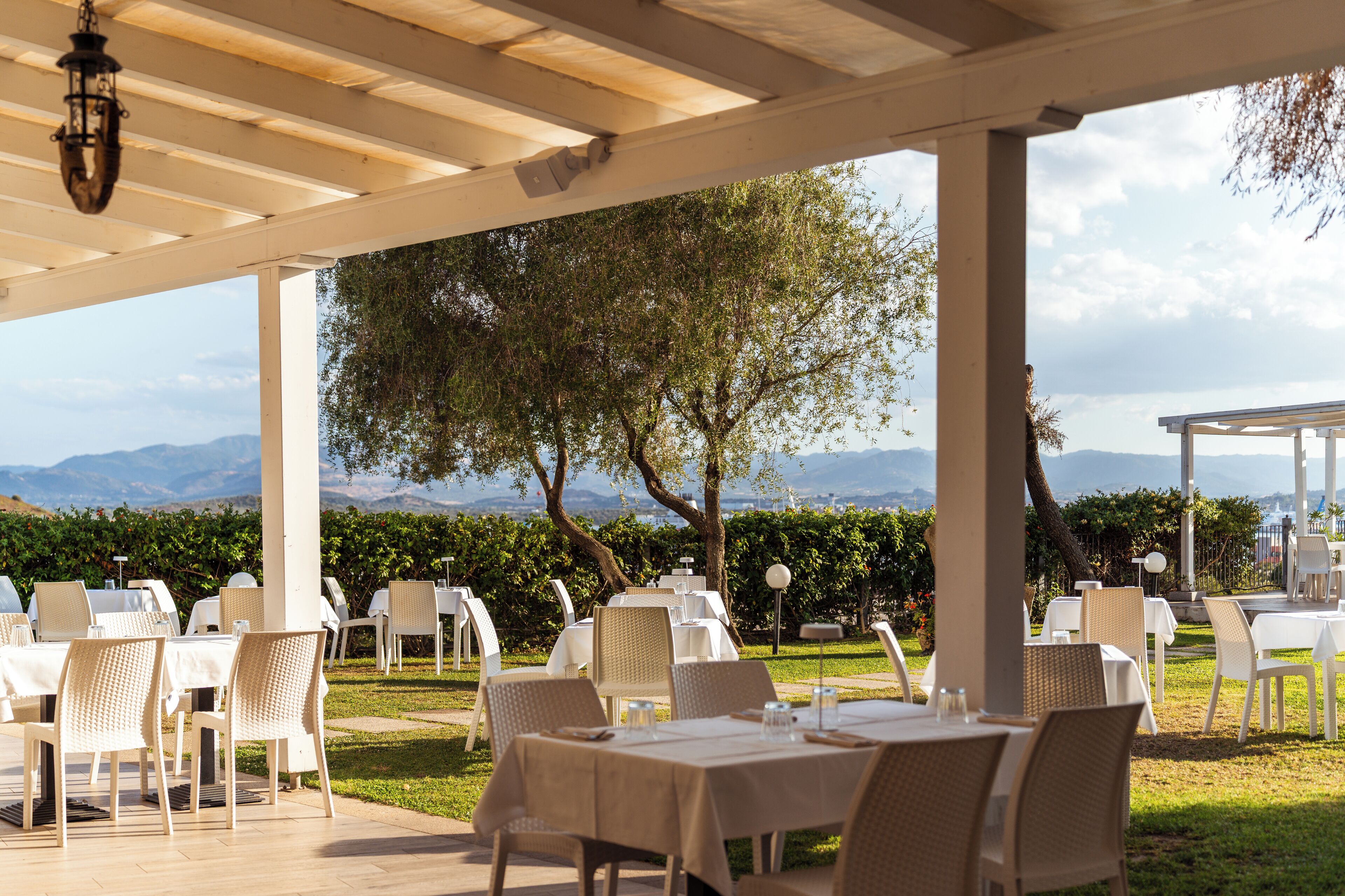 Un espace extérieur aménagé pour les repas, avec des tables et des chaises, une pergola au-dessus et une vue sur le paysage.