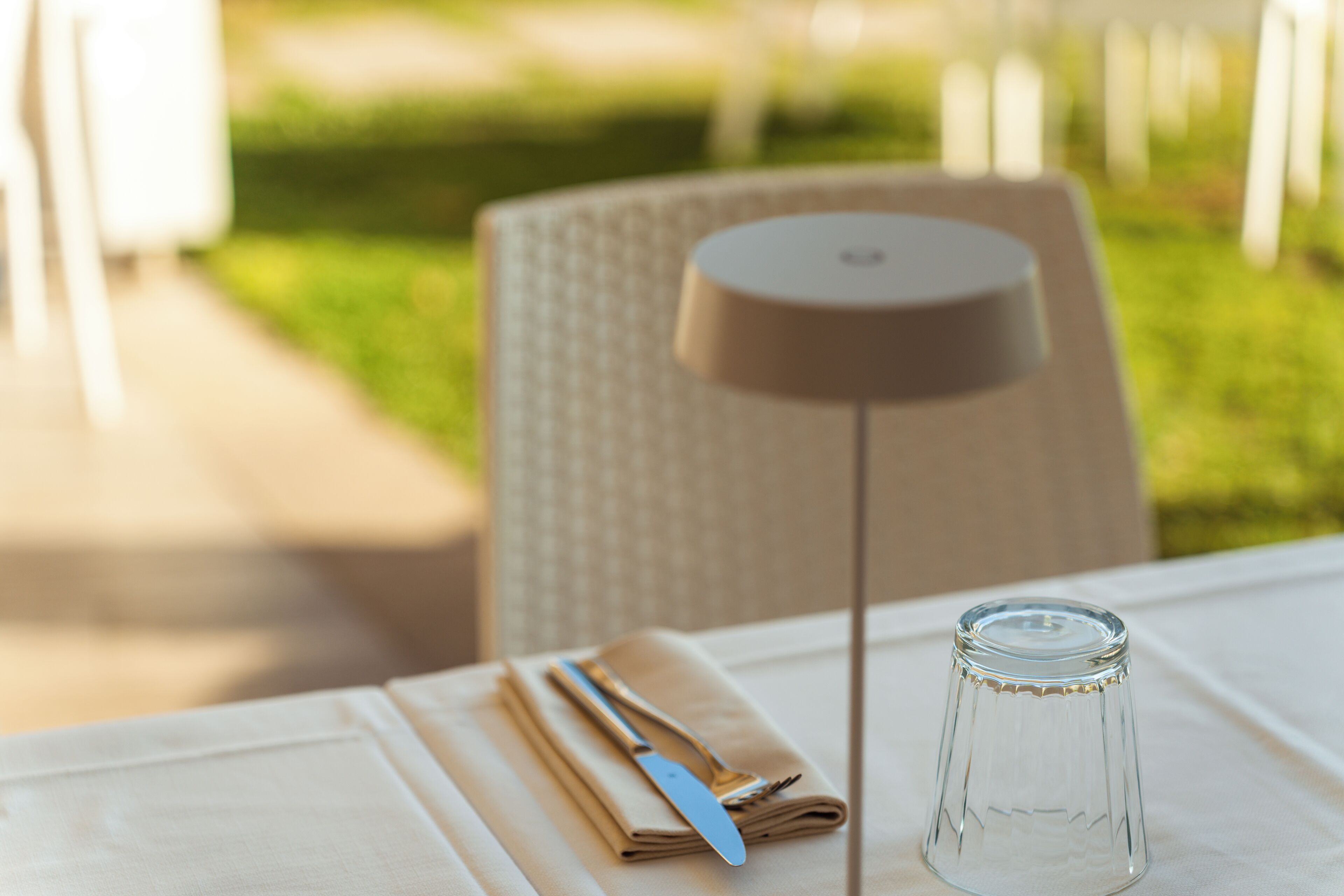 A table set outdoors with a folded napkin, a knife, and a fork, and a clear glass bottle.