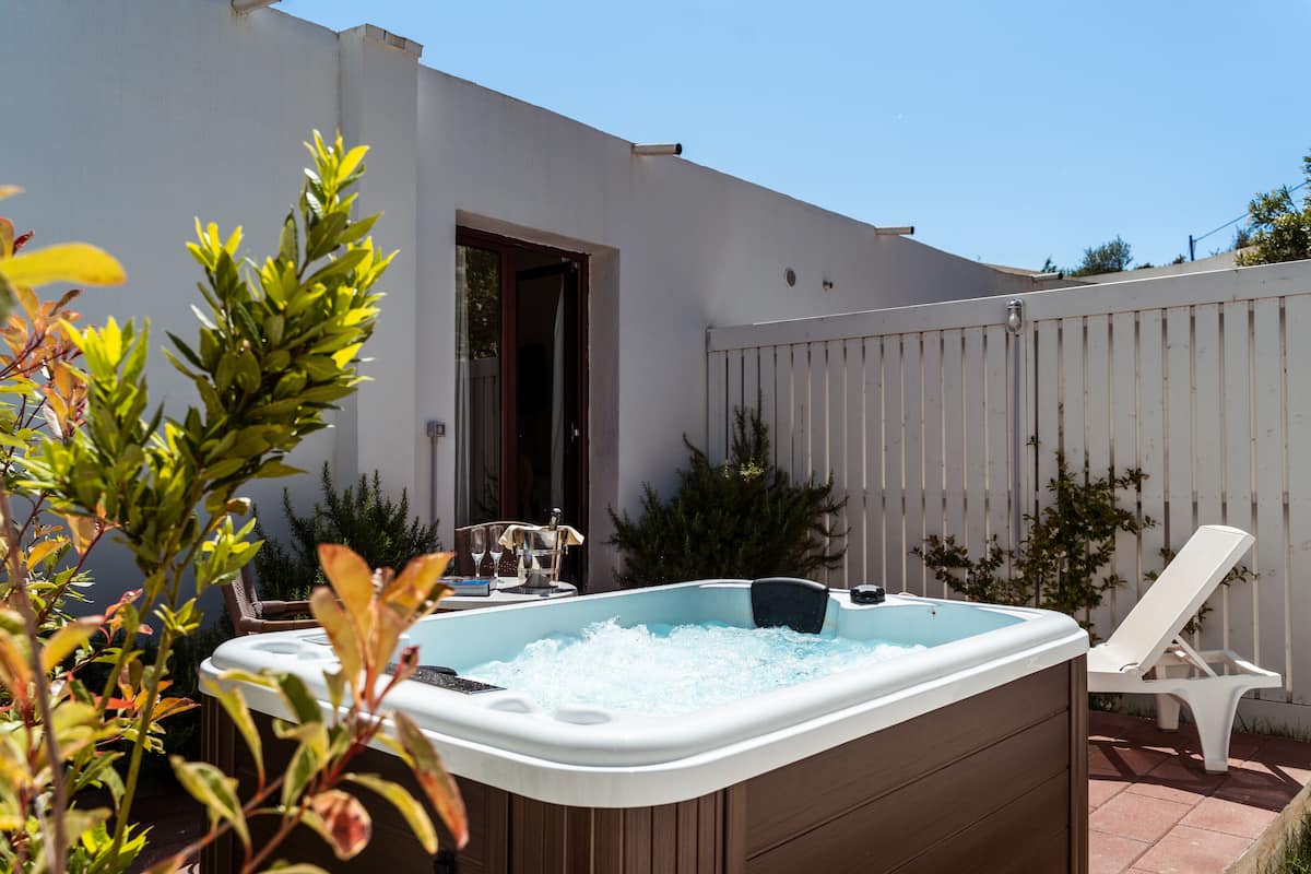A hot tub in a backyard with a white fence, a chair, and some plants.