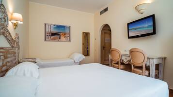 A hotel room with two beds, a desk with chairs, a television, and a painting on the wall.