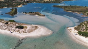 Vista aérea de uma área costeira com águas claras, praias de areia e vegetação dispersa.
