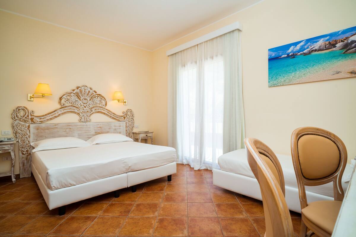 A hotel room with a large bed, two bedside tables with lamps, a chair, and a painting of a beach scene on the wall.