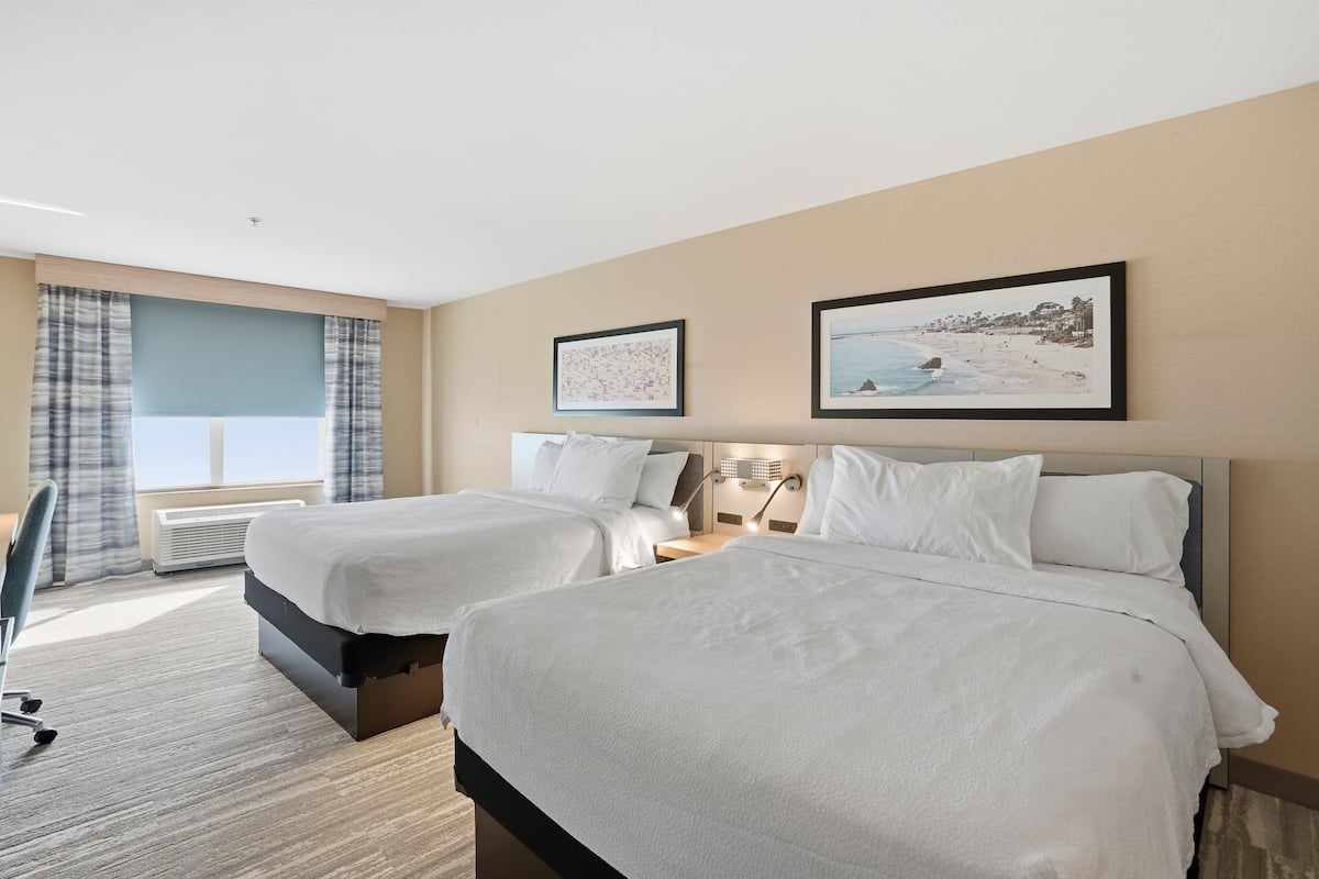 Hotelkamer met twee bedden, een bureau, een stoel, een raam met gordijnen en twee ingelijste foto's aan de muur.
