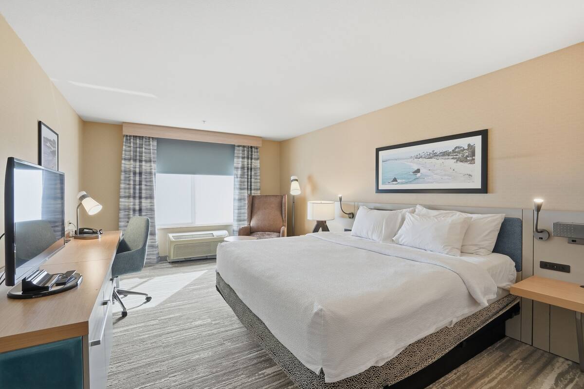 Een hotelkamer met een bed, bureau, stoel, televisie en een schilderij aan de muur.