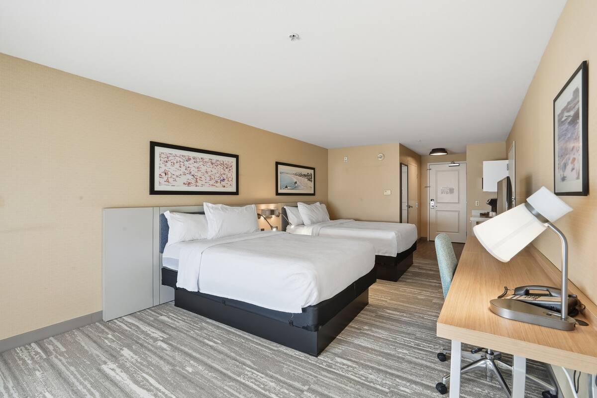 Een hotelkamer met een groot bed, twee kleinere bedden, een bureau met een lamp en kunst aan de muren.