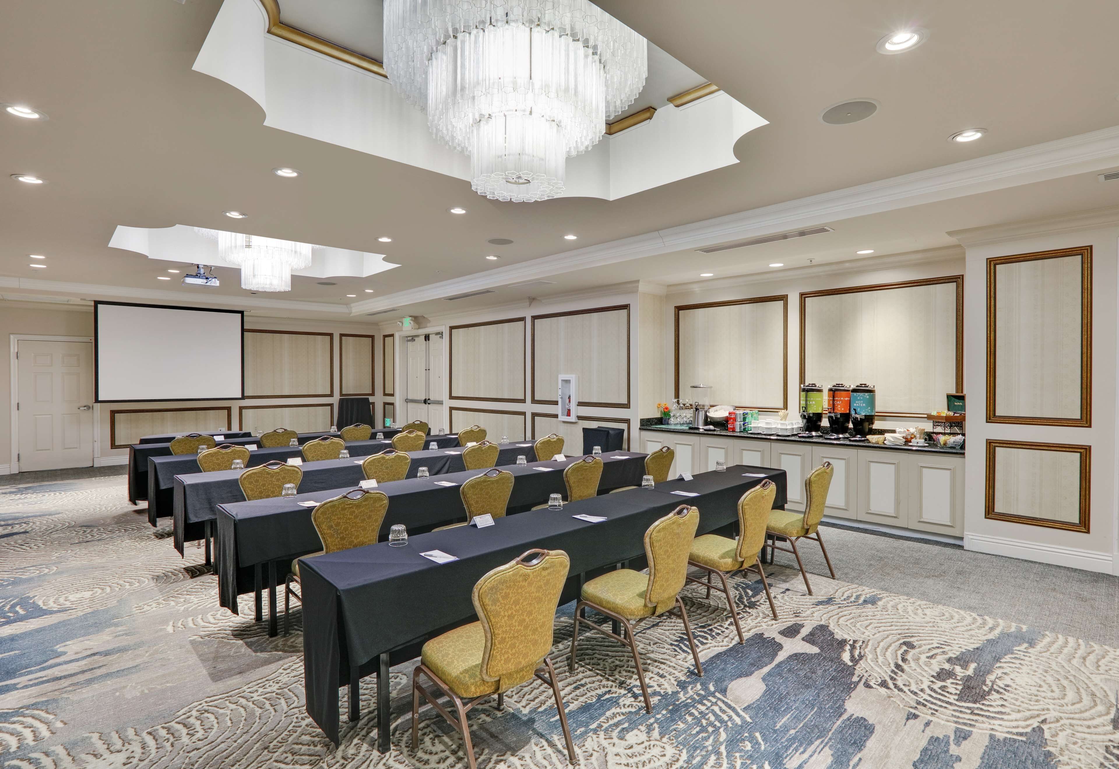 A conference room with long tables, chairs, a projector screen, and a bar area.
