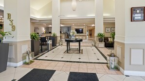 A spacious lobby with a central round table, multiple seating areas, and a reception desk.