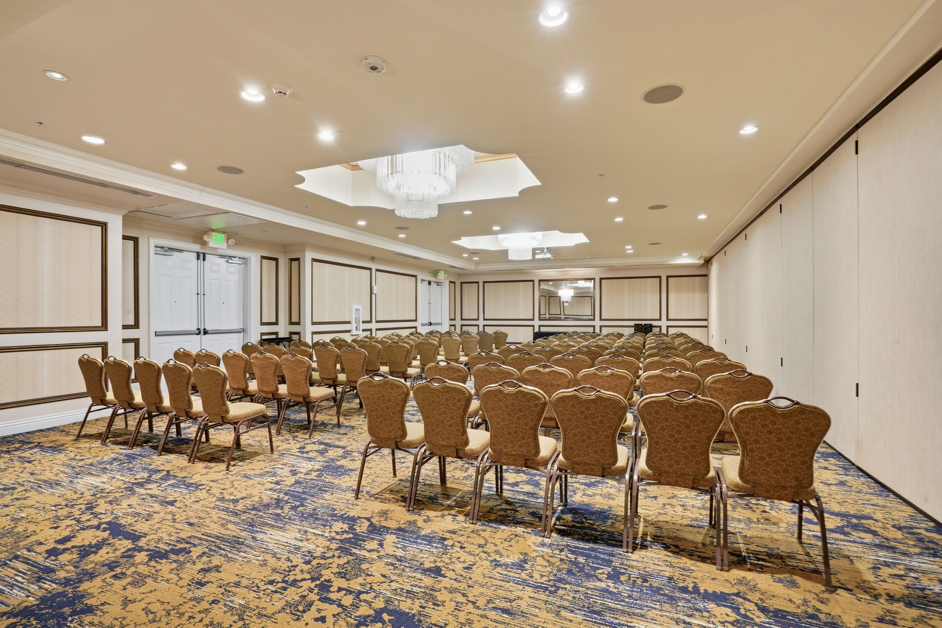 A conference room with rows of chairs, a patterned carpet, and a chandelier.