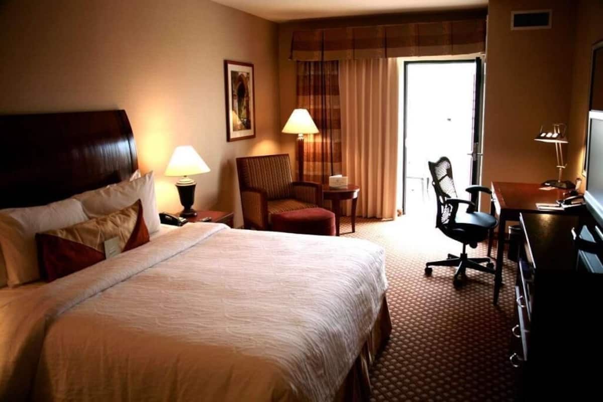 Een hotelkamer met een groot bed, een bureau, een stoel, een lamp en een schilderij aan de muur.