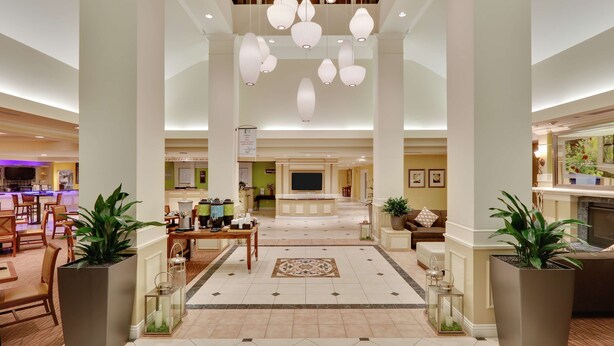 A spacious lobby with a central reception desk, multiple seating areas, and hanging pendant lights.