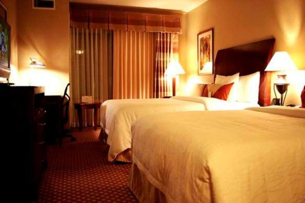 Een hotelkamer met twee bedden, een bureau, een stoel en een raam met gordijnen.