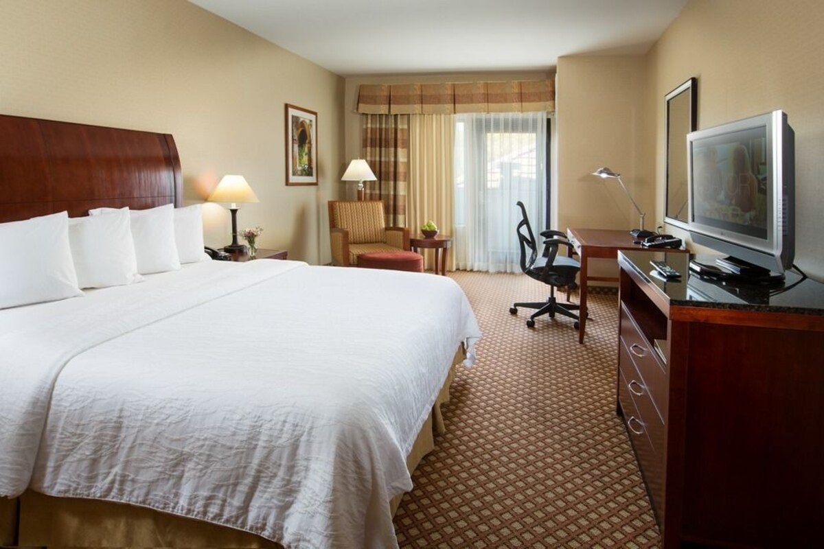 A hotel room with a large bed, a desk with a computer, a television, and a chair.