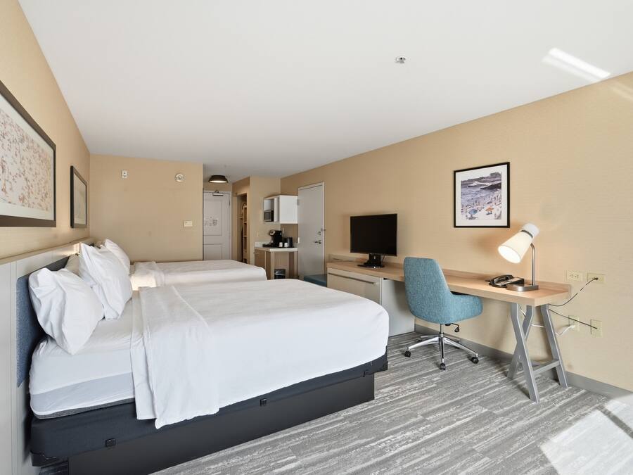 A hotel room with a bed, desk, chair, and a television.