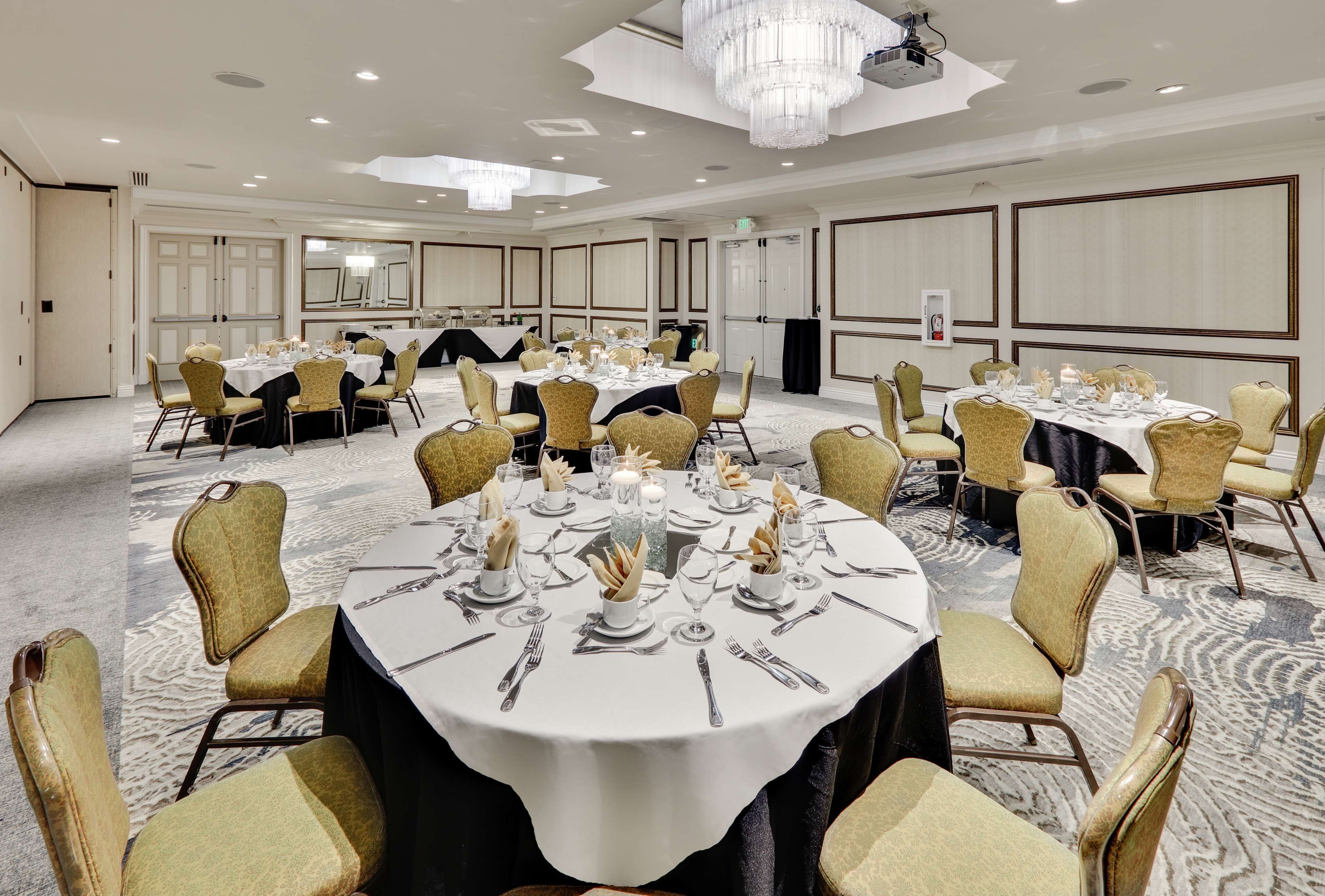 A banquet hall with round tables, gold chairs, and chandeliers.