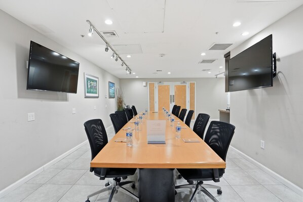 A conference room with a long table, black chairs, water bottles, a projector screen, and a TV mounted on the wall. - Hilton Garden Inn San Diego Del Mar (San Diego)